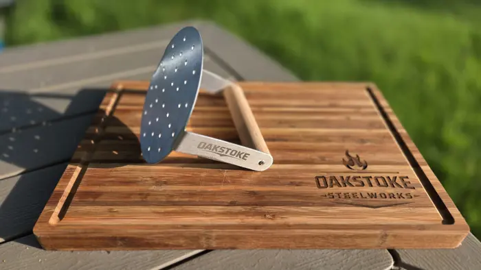 OakStoke Smash Burger Press, full view showing stainless steel perforated disc and hardwood handle on OakStoke cutting board