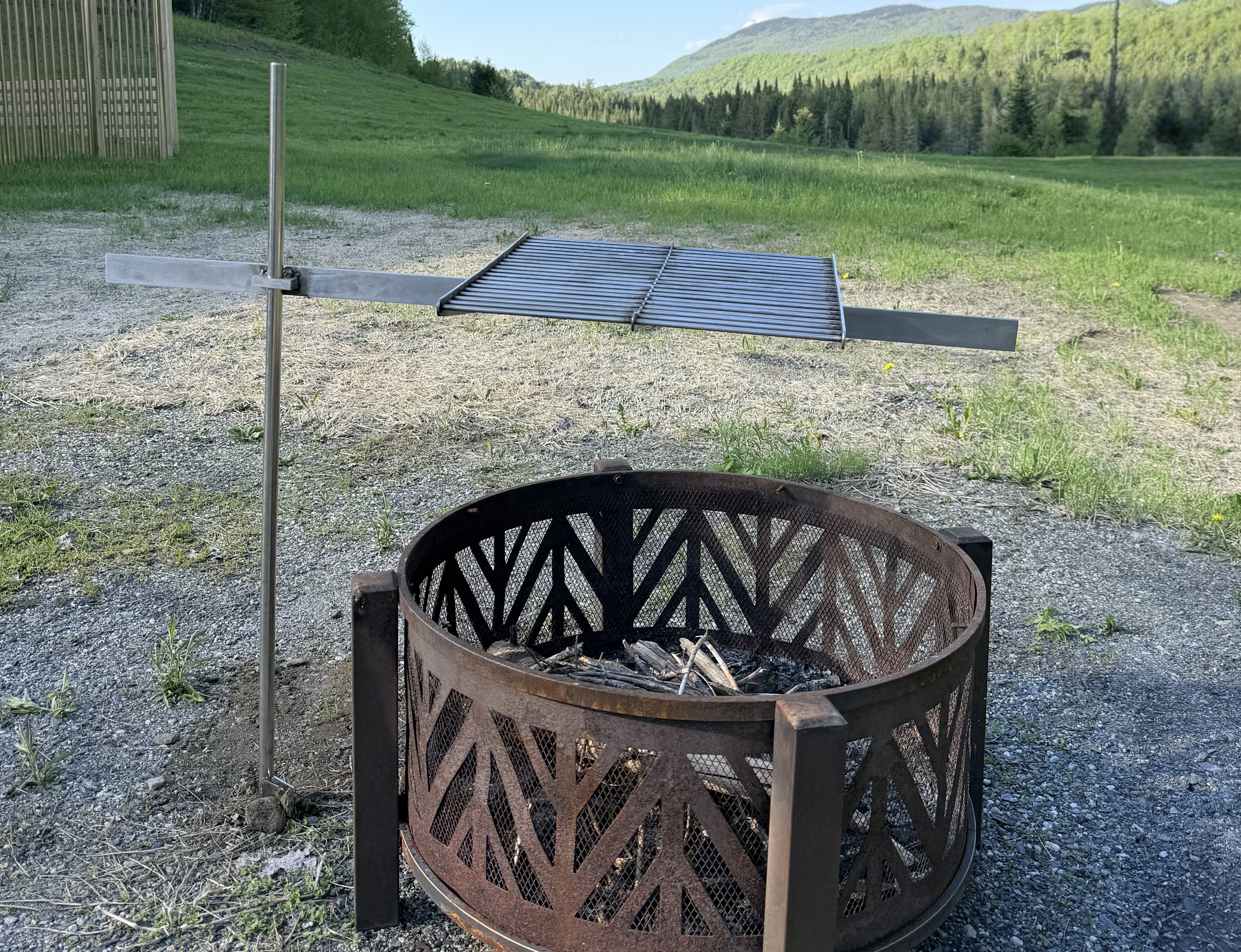 OakStoke Campfire Swivel Arm installed next to fire pit with grill grate extended over the fire, stainless steel campfire grill stand